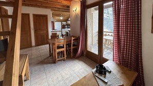 Une pièce chaleureuse avec un plafond en bois, un coin repas avec une table et des chaises, une petite cuisine et une porte-fenêtre coulissante donnant sur un espace extérieur.
