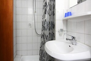 Um banheiro com pia branca, chuveiro com cortina quadriculada preta e branca, e parede revestida de azulejos brancos.