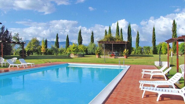 Ein rechteckiger Pool mit einer gefliesten Kante, umgeben von einer Ziegelterrasse. Weiße Liegestühle sind am Poolrand aufgereiht.