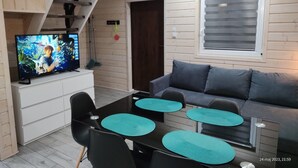 Ein gemütliches Wohnzimmer mit Fernseher, einer Couch und einem Essbereich mit Stühlen und einem Tisch.