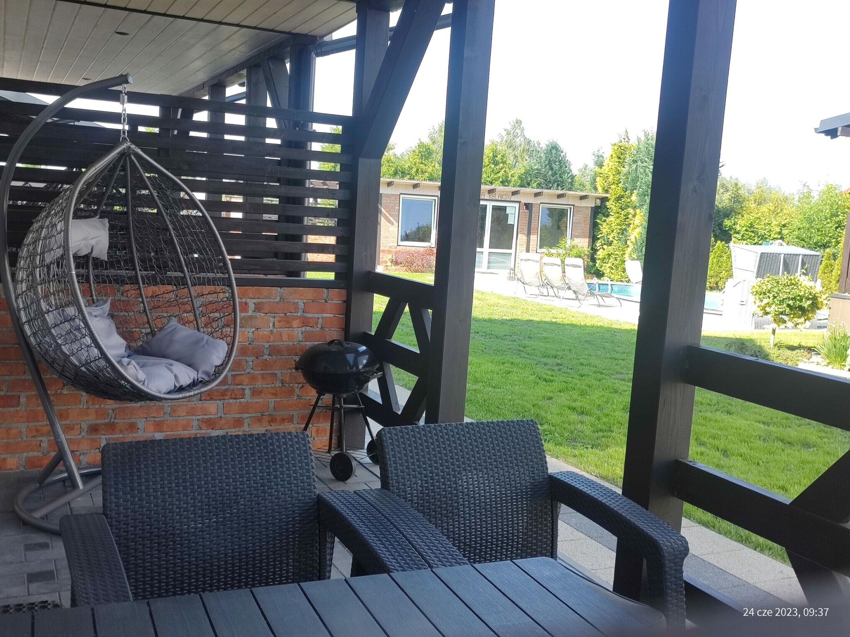 A covered patio with wicker furniture, a hanging chair, and a barbecue grill.
