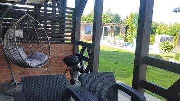 A covered patio with wicker furniture, a hanging chair, and a barbecue grill.