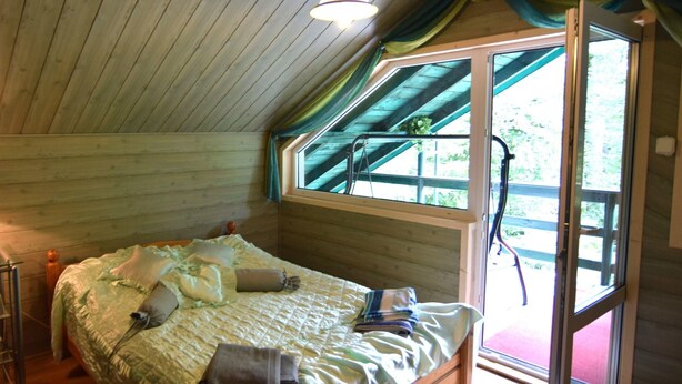 A wooden room with a bed, a window, and a hanging light fixture. - Holiday Home in Zakowo Near Lake (Suleczyno)
