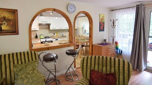 Un salon avec deux fauteuils à rayures, une table à manger en bois et, au fond, une cuisine.