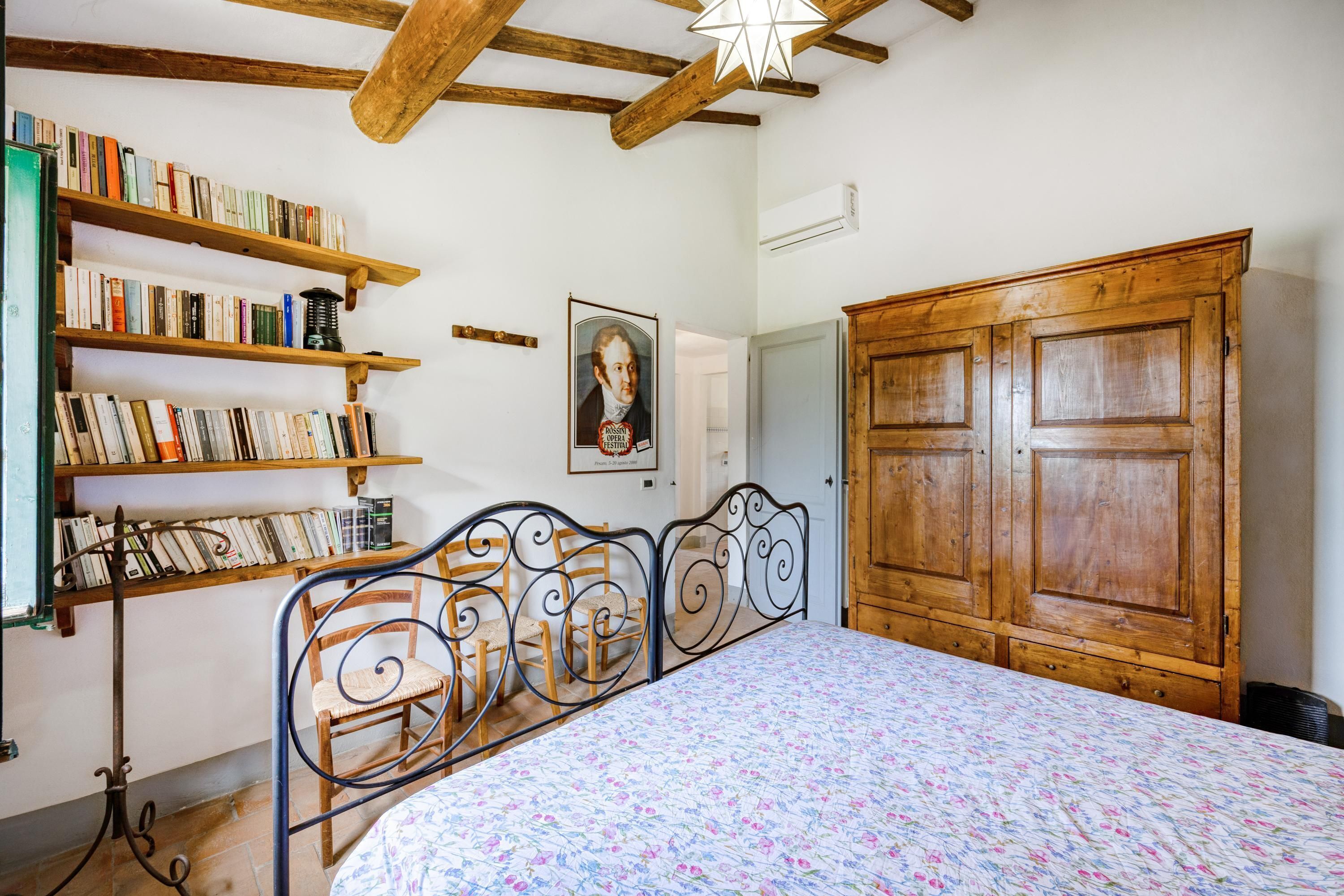 Une chambre à coucher avec un lit en métal, des étagères en bois remplies de livres, une armoire en bois et un tableau encadré accroché au mur.