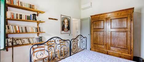 Une chambre à coucher avec un lit en métal, des étagères en bois remplies de livres, une armoire en bois et un tableau encadré accroché au mur.