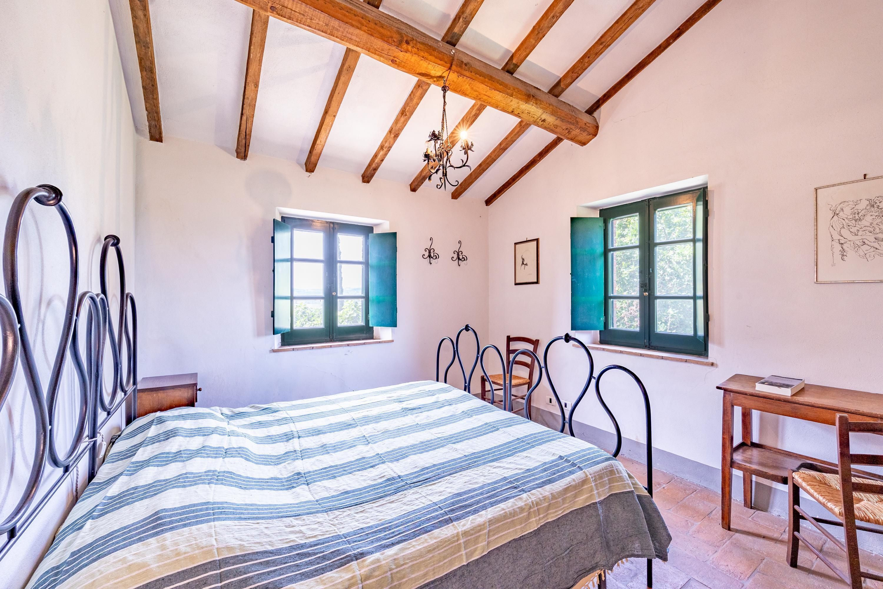 A bedroom with a bed, a wooden table, two chairs, a window, and a chandelier.