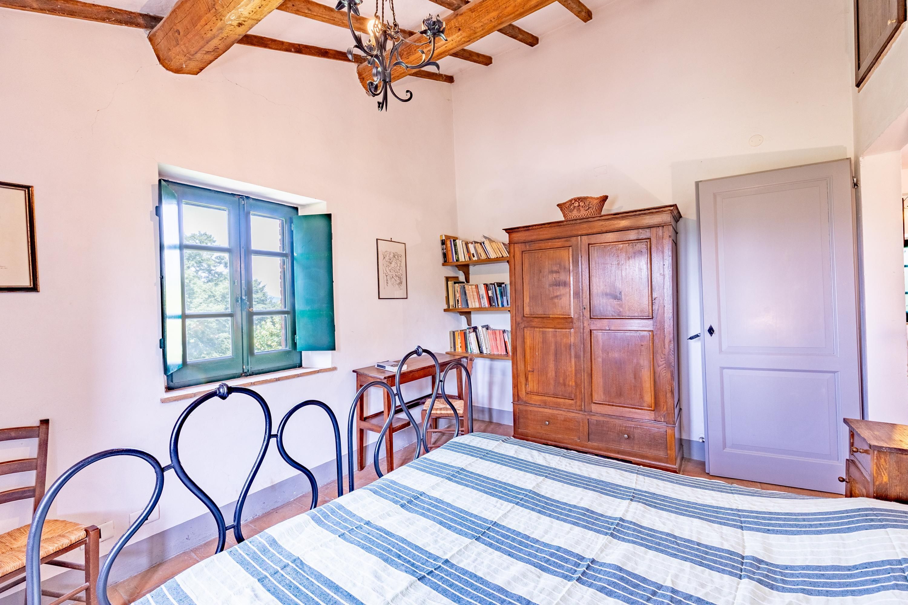 A bedroom with a bed, wooden furniture, a window, and a chandelier.