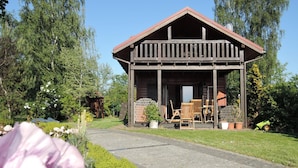 A wooden cabin with a porch, surrounded by a garden and trees. - Holiday Home Kolczewo Near Baltic Sea Beach (gmina Wolin)