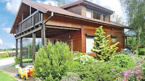 A two-story wooden house with a balcony, surrounded by lush greenery and a small play area with toys. - Holiday Home Kolczewo Near Baltic Sea Beach (gmina Wolin)