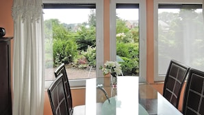 A dining area with a glass table and black chairs, a vase with flowers, and a view of greenery and buildings through large windows. - Holiday Home Kolczewo Near Baltic Sea Beach (gmina Wolin)