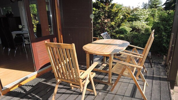 A wooden deck with a round table and chairs, a wooden door, and a view of greenery. - Holiday Home Kolczewo Near Baltic Sea Beach (gmina Wolin)
