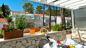 Un'area pranzo all'aperto con un muro in pietra, piante in vaso, un tavolo apparecchiato con una bottiglia, anguria, uva e una ciotola di frutta.