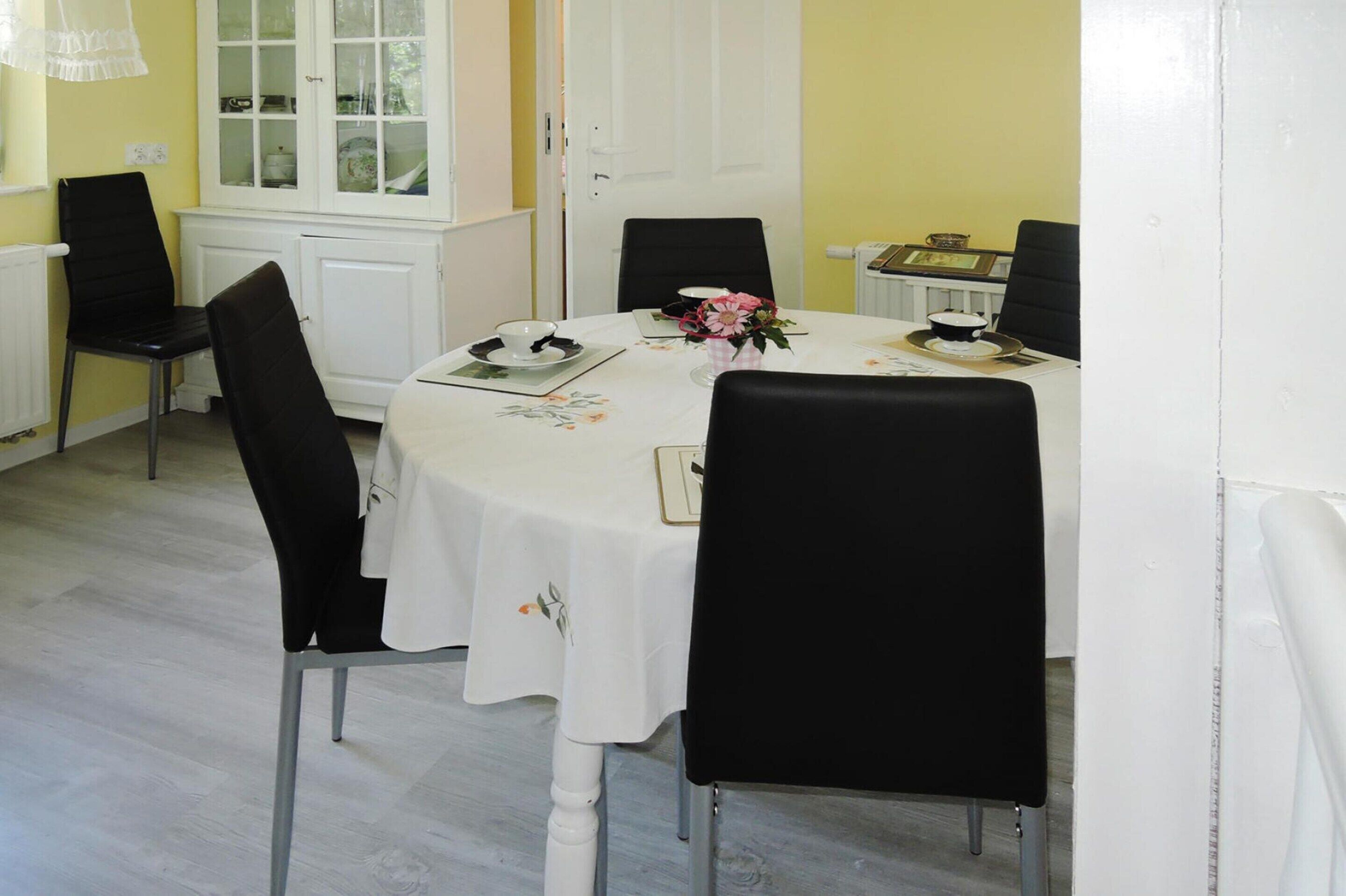 Un comedor con una mesa redonda, sillas negras, un mantel blanco y un aparador con puertas de cristal.