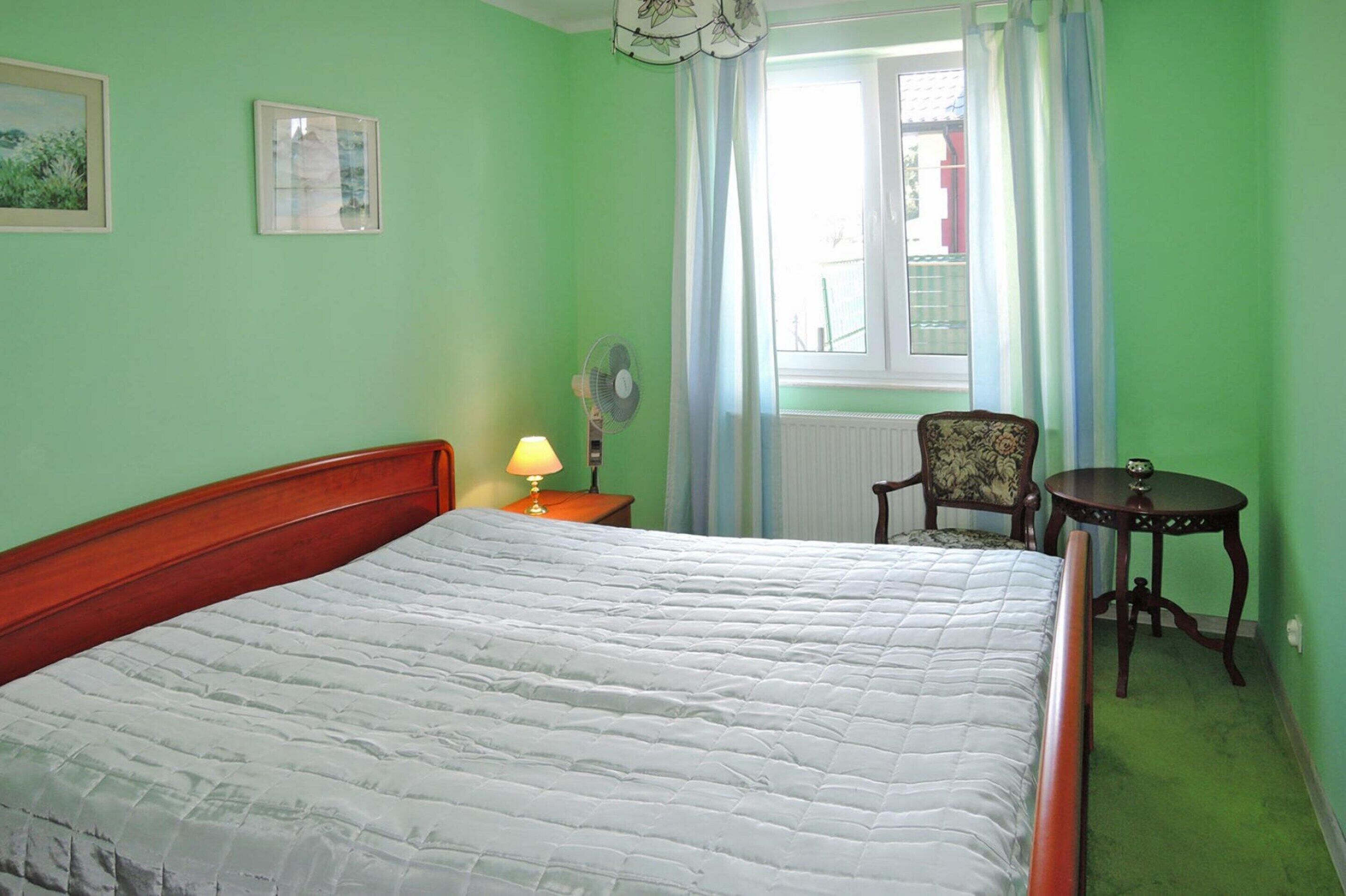 Une pièce comprenant un lit, une chaise, une table, une lampe et une fenêtre avec des rideaux.