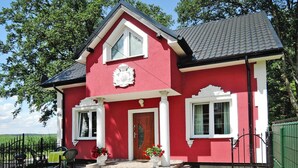 A red house with a white door, two windows, and a coat of arms above the door. - New Holiday Home in Nowe Warpno for 6 Persons (Nowe Warpno)