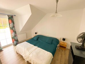 A bedroom with a bed, a desk, a chair, a radiator, a window with curtains, and a ceiling fan. - Holiday Home in Nowe Warpno Near Harbor (Nowe Warpno)