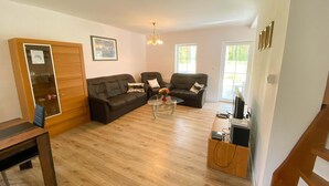 A living room with a wooden floor, two sofas, a glass coffee table, and a TV stand. - Holiday Home in Nowe Warpno Near Harbor (Nowe Warpno)
