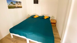 A single-bed room with a teal bedspread, two pillows, a nightstand with a lamp, and a wall-mounted light fixture. - Holiday Home in Nowe Warpno Near Harbor (Nowe Warpno)