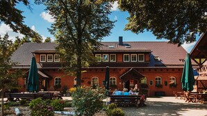 A traditional brick building with a tiled roof, outdoor seating area with tables and benches, and a garden with various plants and flowers.