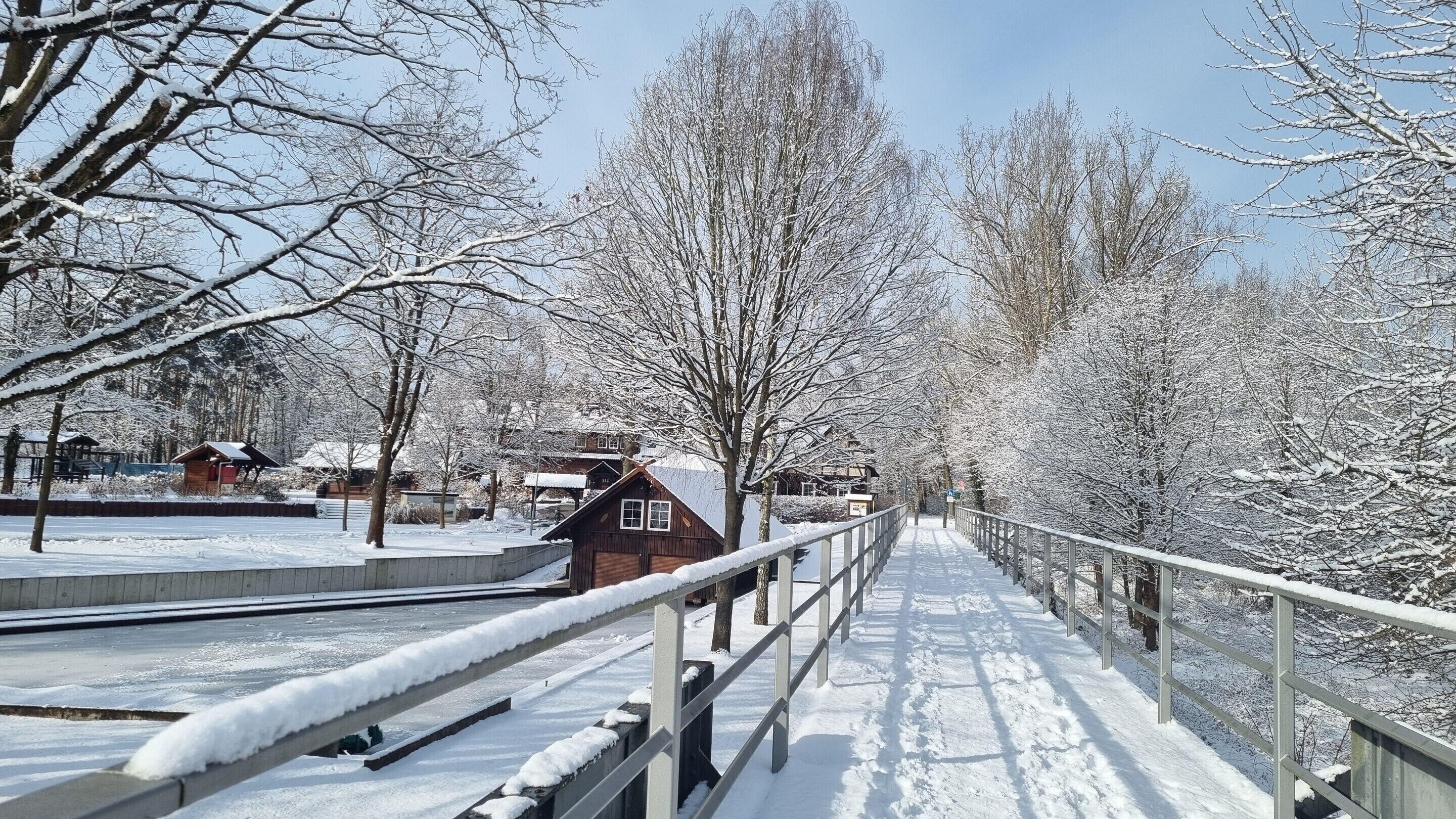 Un sendero cubierto de nieve con una valla de madera y un pequeño edificio.