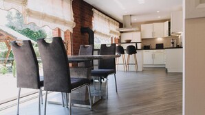 A modern dining area with a brick wall, a large window with curtains, and a kitchen in the background.