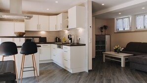 A modern kitchen with white cabinets, a black countertop, and a built-in oven. There is a dining area with two black chairs and a small table.
