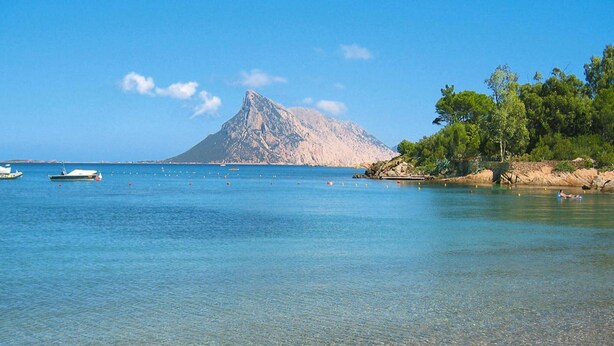A beach with clear shallow waters, boats, and a mountain in the background. - Apartment in Monte Petrosu Near San Teodoro (San Teodoro)