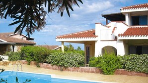 A swimming pool with a white building in the background, surrounded by greenery. - Apartment in Monte Petrosu Near San Teodoro (San Teodoro)