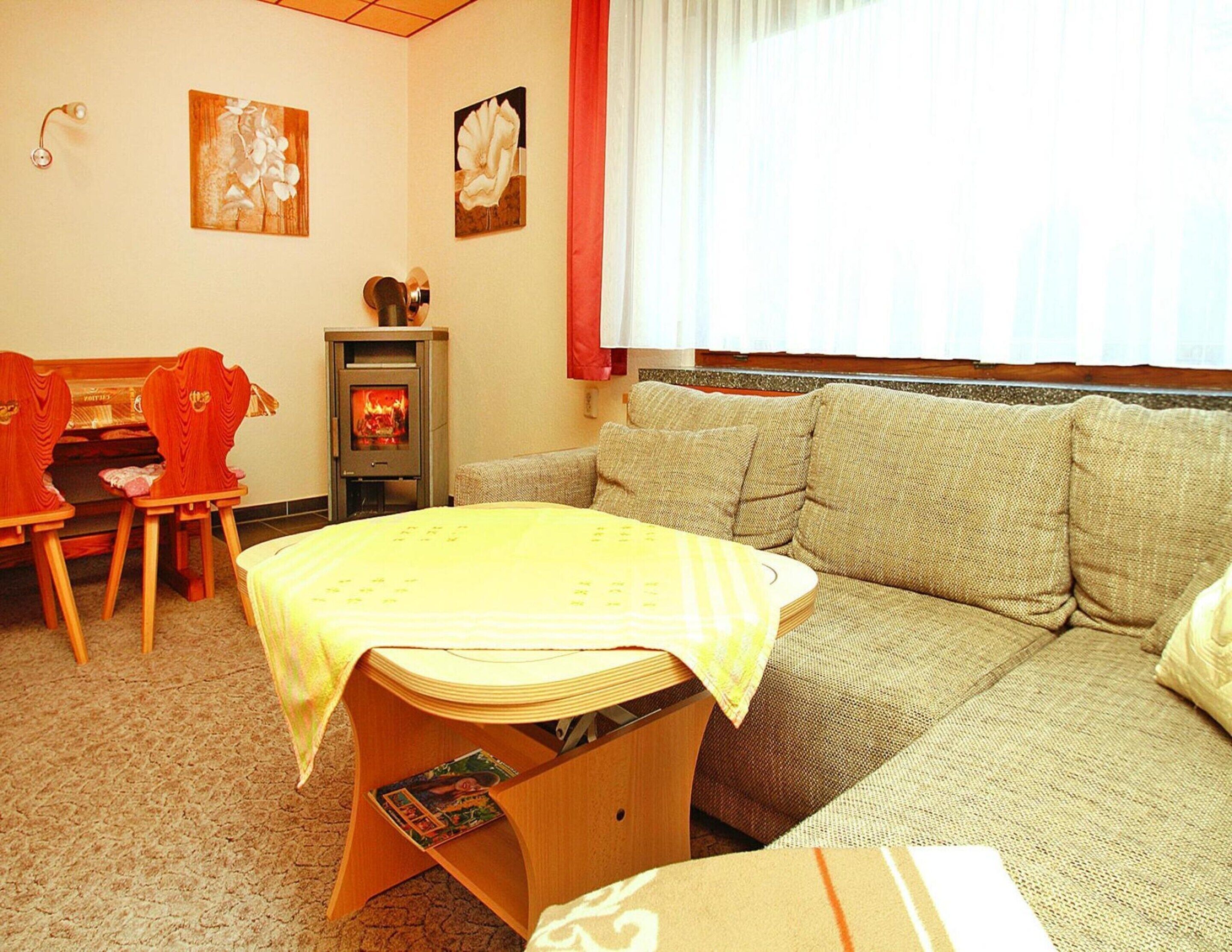 Een gezellige woonkamer met een bank, een klein houten tafeltje met een gele tafelkleed, een open haard en twee stoelen.