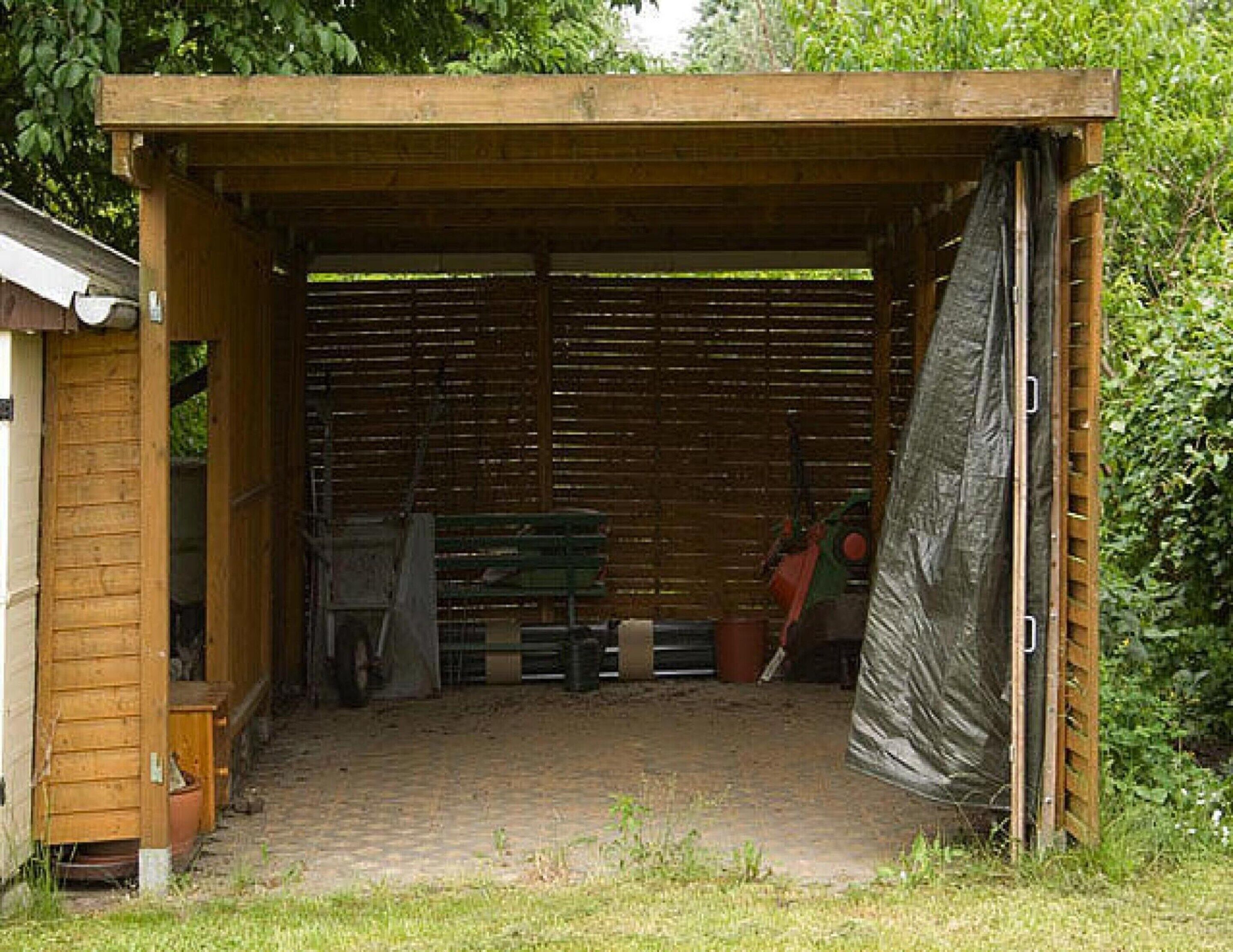 A wooden shed with a slanted roof, a brick floor, and a green bench inside.