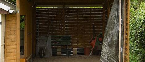 A wooden shed with a slanted roof, a brick floor, and a green bench inside.
