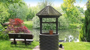 Un belvédère doté d’une base en pierre et d’un toit en pente, entouré d’une végétation luxuriante et bordé d’un étang.