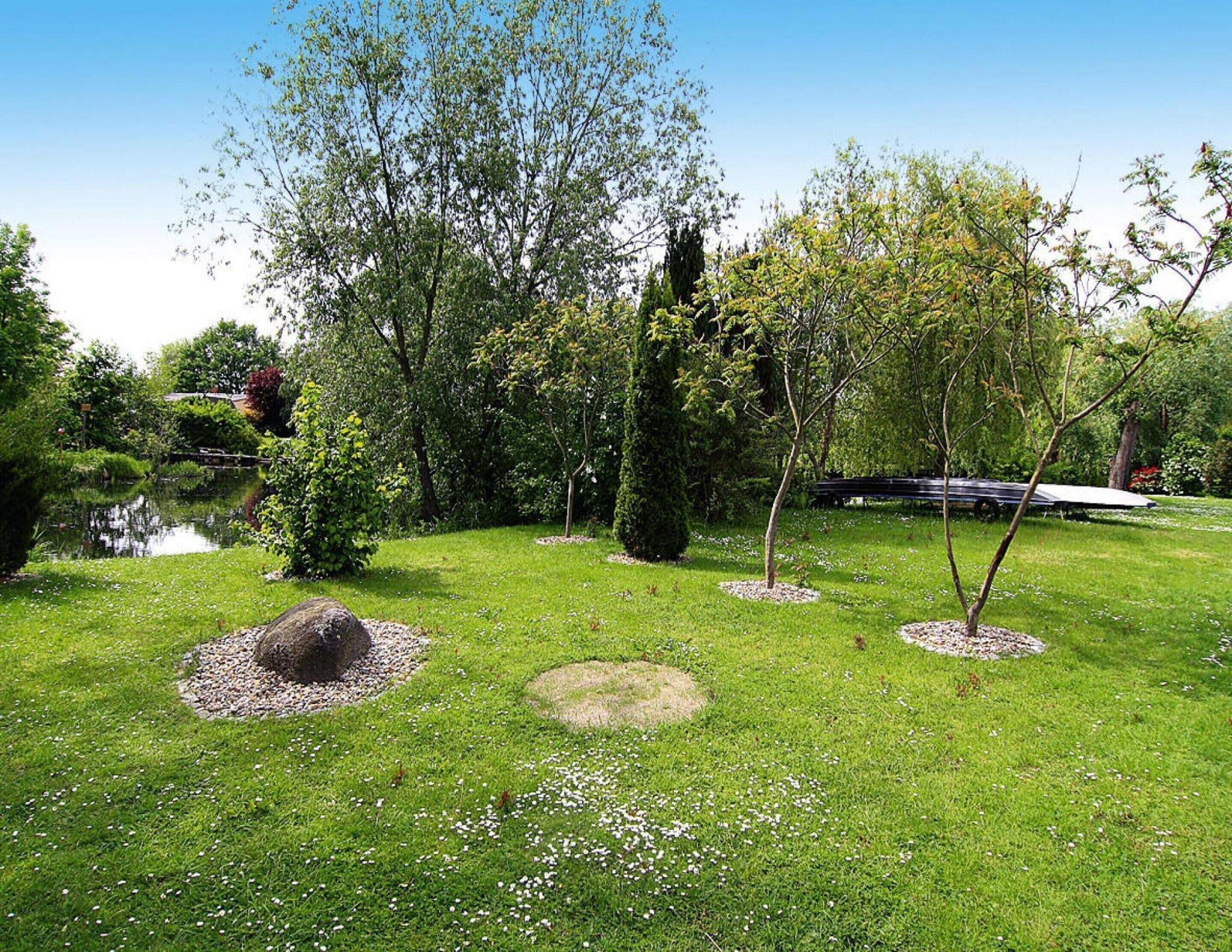 A well-maintained garden with a pond, various trees, and a bench.