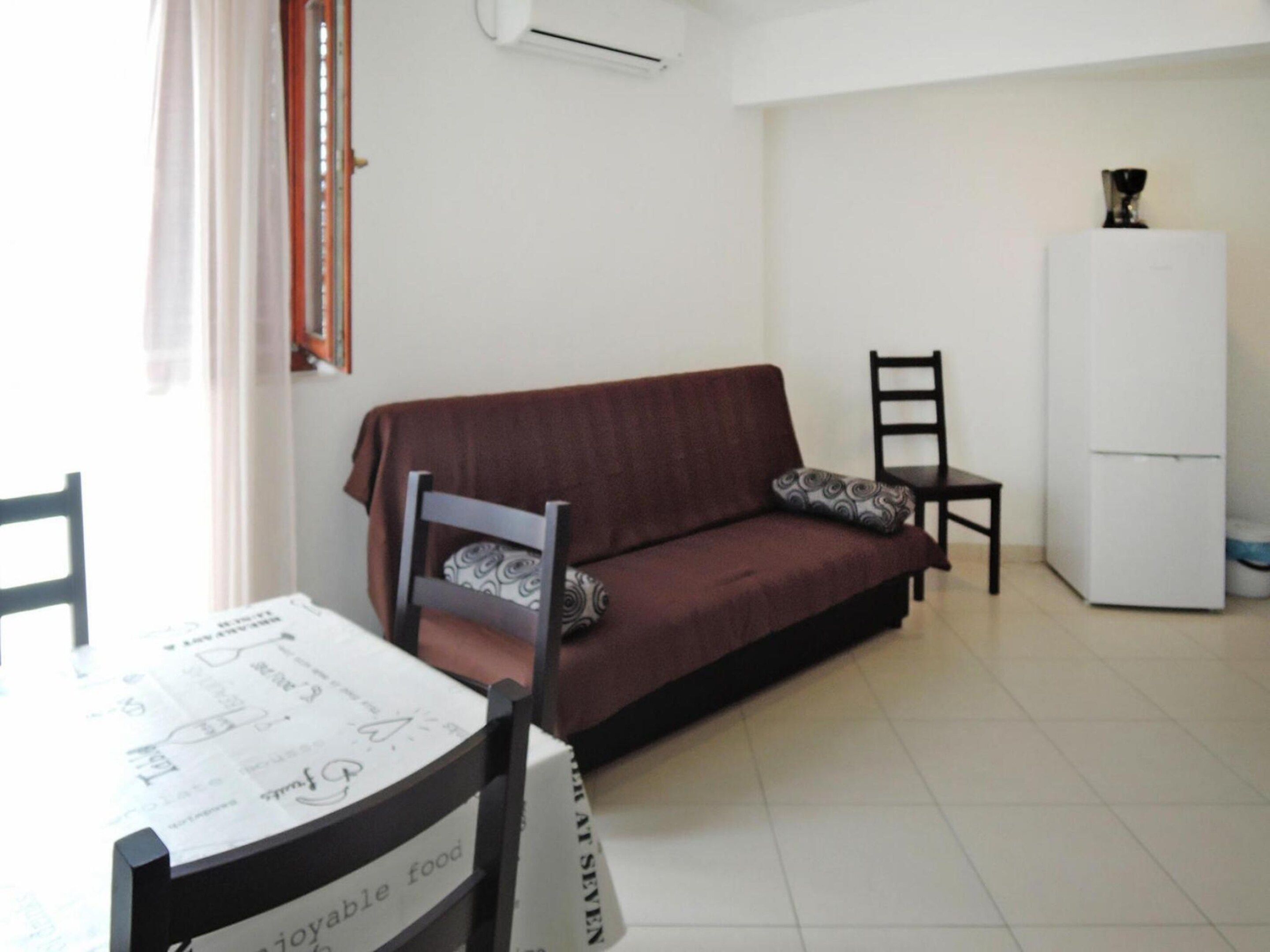 A living room with a sofa, a dining table with a menu, and a white refrigerator.