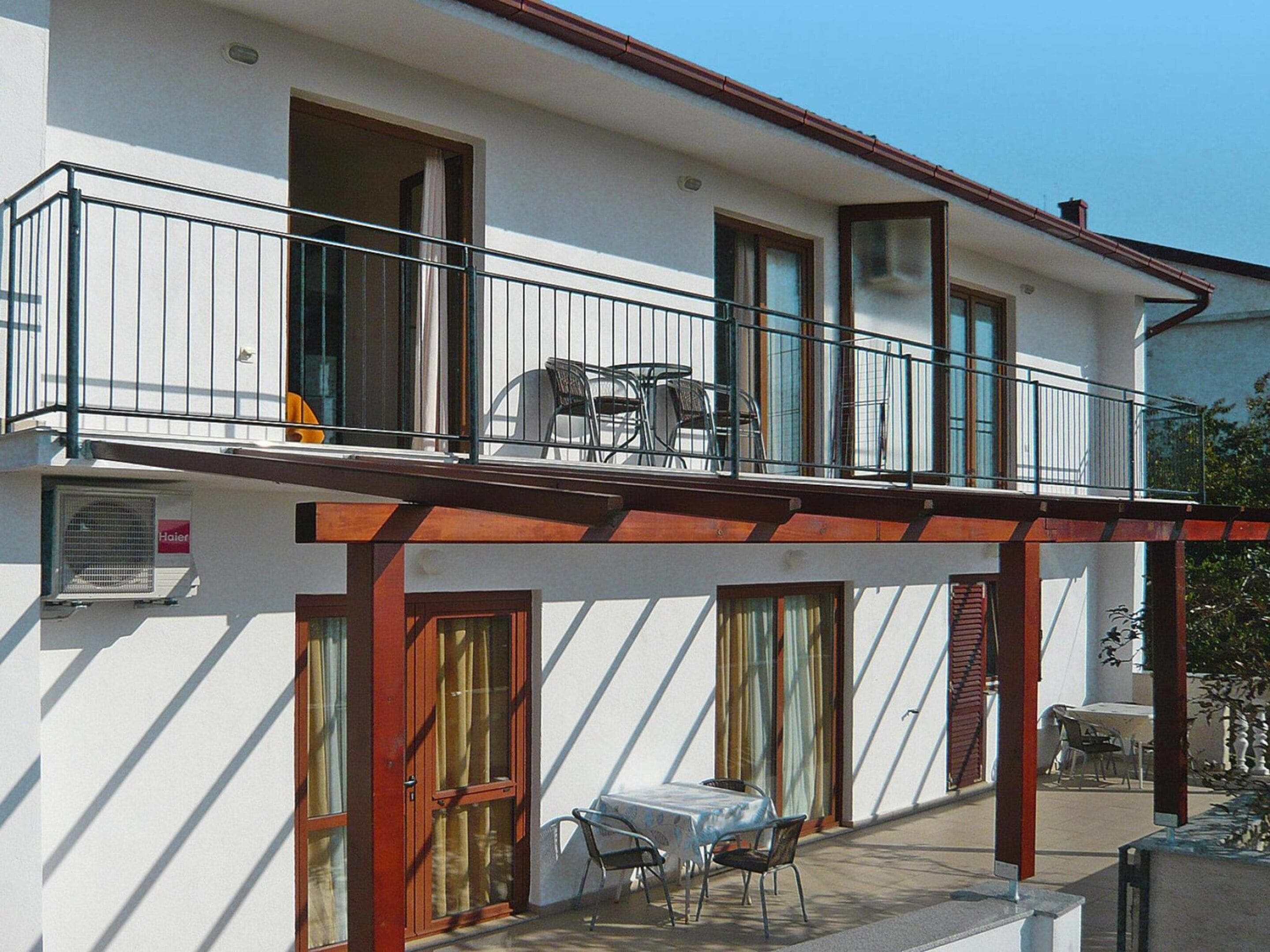 A two-story building with a balcony, a table and chairs outside, and a door with a window.