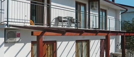A two-story building with a balcony, a table and chairs outside, and a door with a window.
