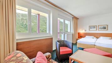 A hotel room with a sofa, a chair, a bed, and a table. There are windows with a view of a green landscape.