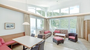 Una habitación amplia con una gran mesa de comedor, dos sofás y una silla. Amplias ventanas ofrecen vistas a colinas verdes.