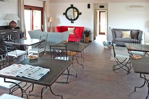 A spacious living area with a red sofa, a grey sofa, and a dining table with chairs. There is a large mirror on the wall and a potted plant on the floor. - Holiday Residence Punta Falcone (Santa Teresa di Gallura)