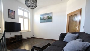 A living room with a dark-colored sofa, a television, a wooden coffee table, and a door. - Ferienwohnung am Aubach in Schwerin (Schwerin)
