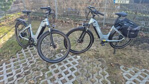 Two electric bicycles parked on a paved area with a brick wall and a metal fence in the background. - Ferienwohnung am Aubach in Schwerin (Schwerin)