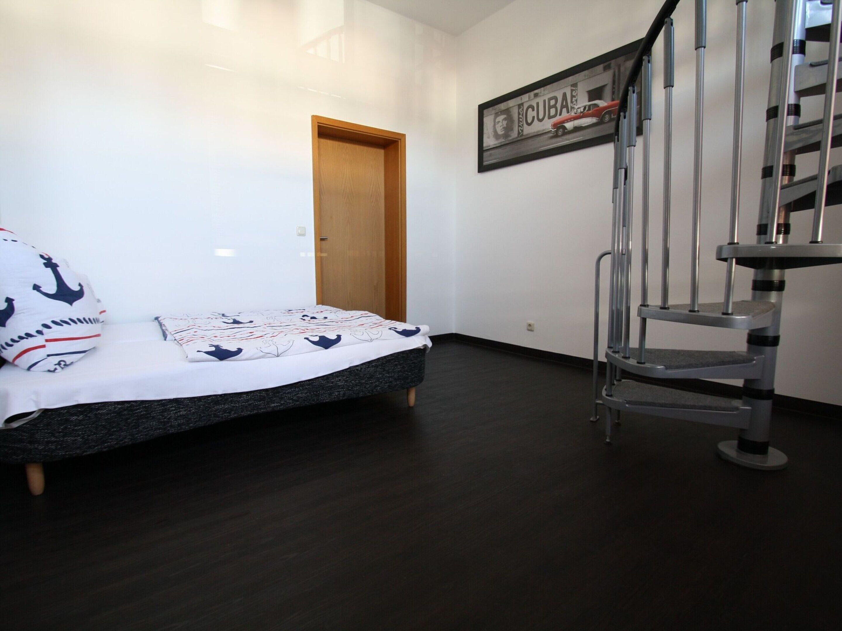 Een slaapkamer met een bed, een houten deur, een trap en een aan de muur hangend schilderij van een auto.