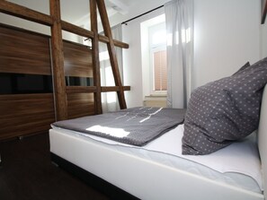 Ein Schlafzimmer mit Etagenbett, einer Stehleiter, einem Fenster mit Vorhängen und einem Nachttisch.