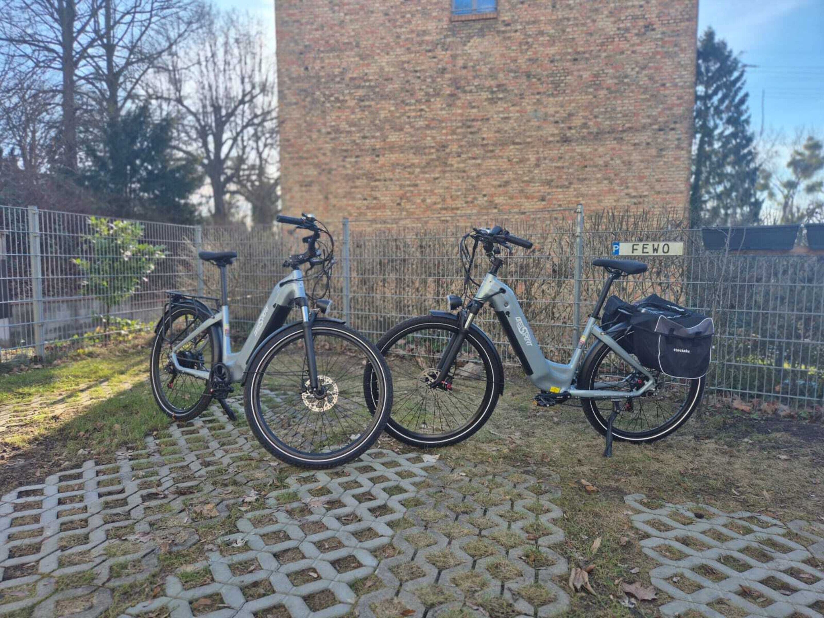 Dos bicicletas estacionadas en un área pavimentada, con un edificio de ladrillo al fondo.