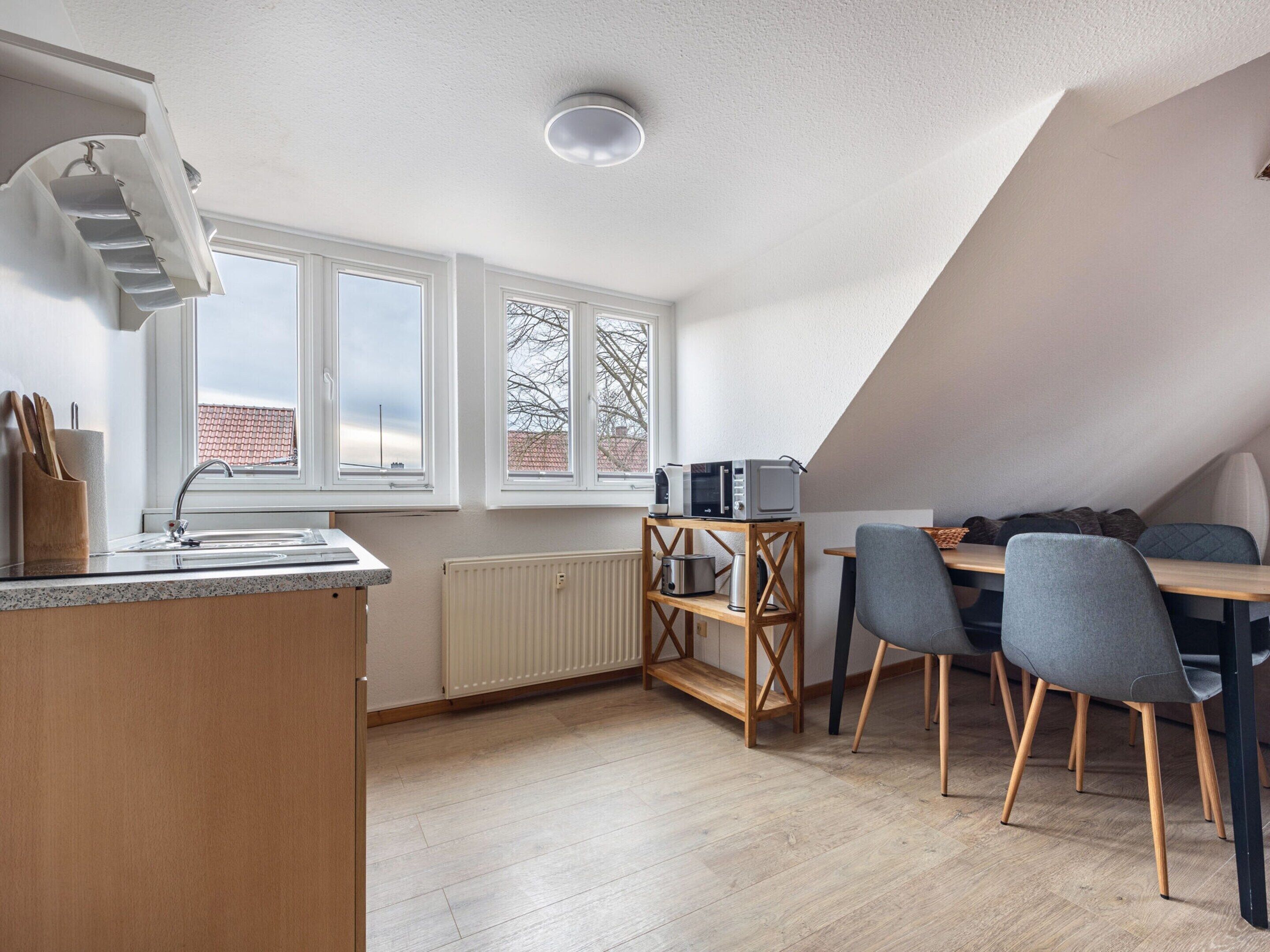 A modern kitchen with a built-in oven, a dining area with a wooden table and chairs, and large windows offering views of the outside.