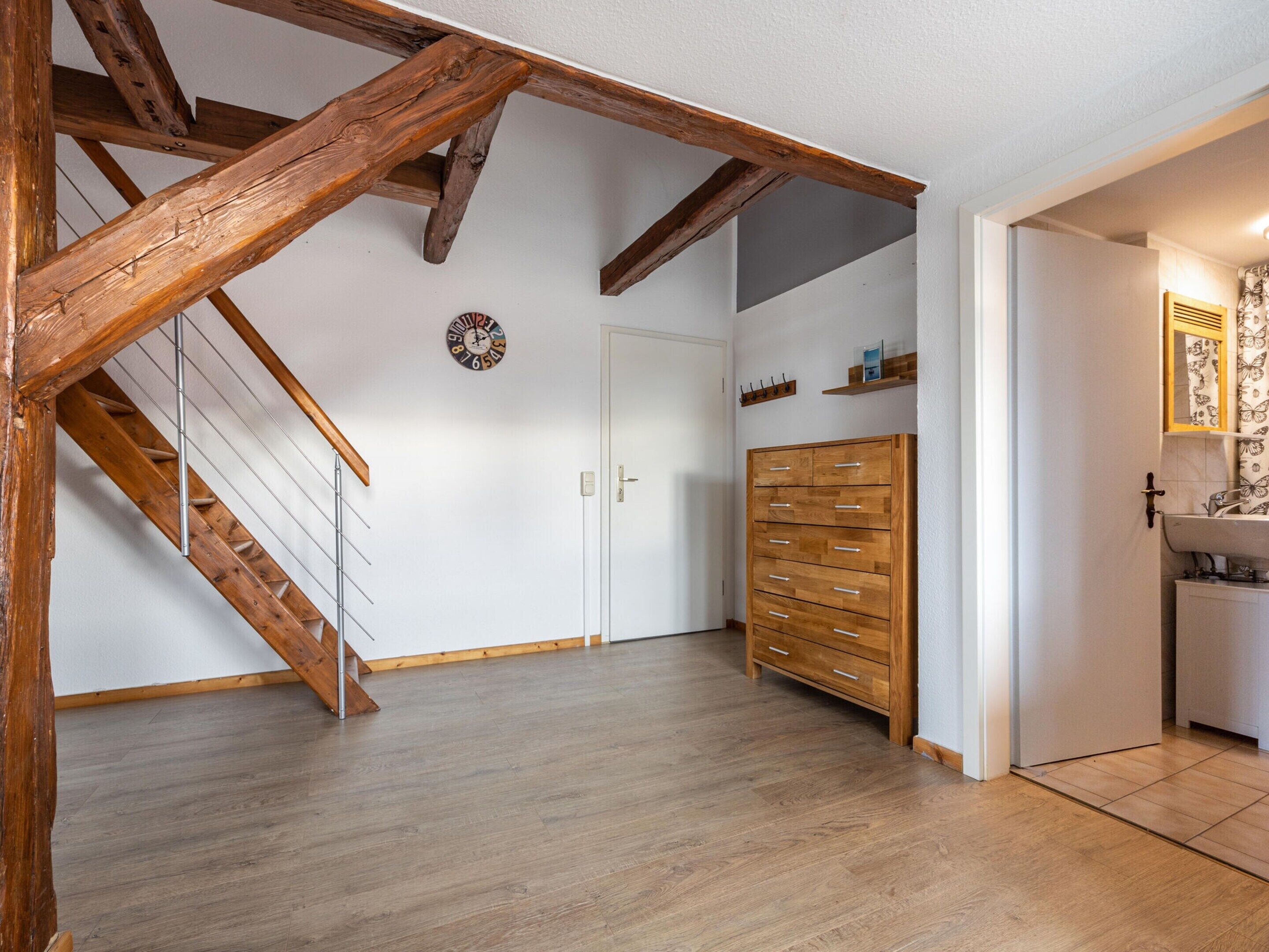 A room with a wooden staircase, a wooden wardrobe, a white door, and a wall clock.