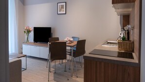 A modern kitchen with a dining area, featuring a flat-screen TV, wooden cabinets, and a small island with a sink. - Nice, Cozy Apartment Very Close to the Beach (Rewal)