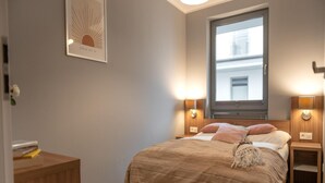A bedroom with a bed, bedside tables, a window, and a wall-mounted light fixture. - Nice, Cozy Apartment Very Close to the Beach (Rewal)
