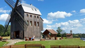 A rustic wooden windmill with a metal roof, a small wooden building with a sloped roof, and a picnic area with benches and tables. - Holiday Home by the Lake, Sauna, Boat, Bicycles (Chmielno)
